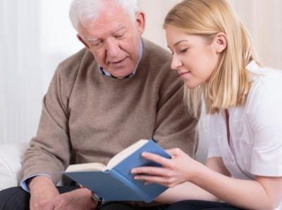 Photograph of an elderly gentleman looking at a book with a young woman