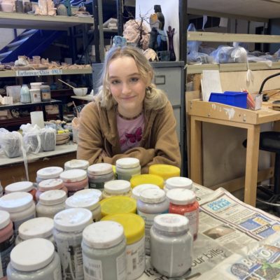 Art student Naomi Hardwick next to pots of paint in the art and design workshop