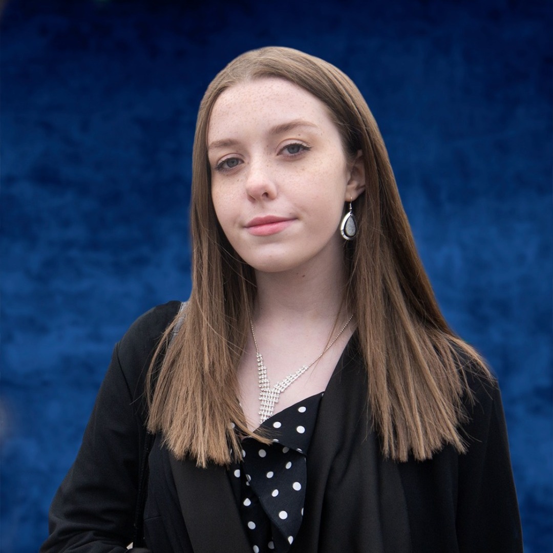 Performing arts student Kacey Howell, wearing a black and white top, standing in front of a dark blue background