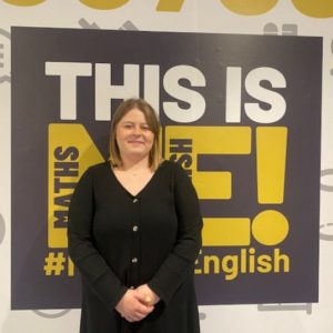 Business sector gateway student Edyta Opolska, wearing a black top and standing in front of a blakc and yellow college sign