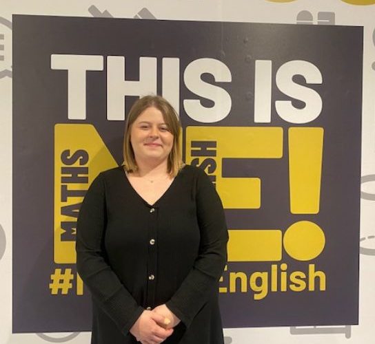 Business sector gateway student Edyta Opolska, wearing a black top and standing in front of a blakc and yellow college sign