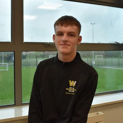 Sports student Daniel Jones wearing a black top with the college logo on the lefthand side, in front of a window overlooking the sports field