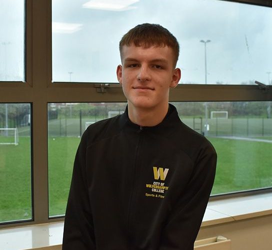 Sports student Daniel Jones wearing a black top with the college logo on the lefthand side, in front of a window overlooking the sports field