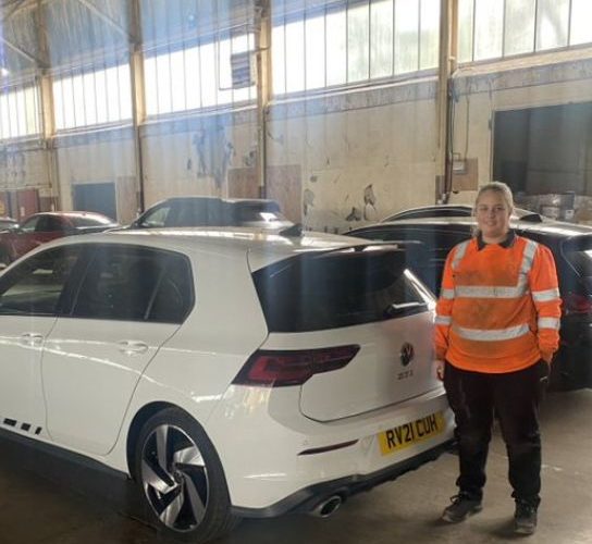 Former motor vehicle student Keri-Leigh Price, wearing a hi-vis jacket and standing next to a white car in the workshop at Greenhous in Shrewwsbury