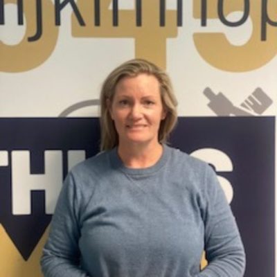 Student Kerry O'Brien wearing a greay top, standing in front of a wgite, yellow and grey decorated wall