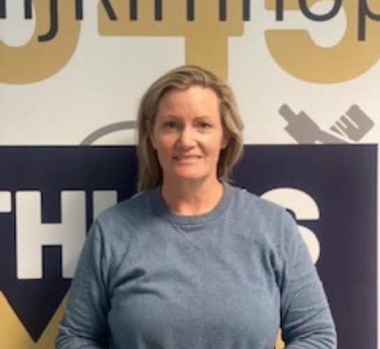 Student Kerry O'Brien wearing a greay top, standing in front of a wgite, yellow and grey decorated wall