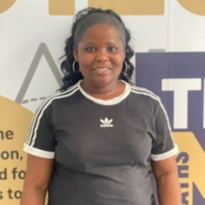 Student Lydia Fosuah wearing a greay t-shirt standing in front of a white, yellow and grey wall