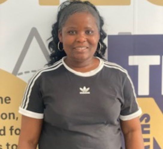 Student Lydia Fosuah wearing a greay t-shirt standing in front of a white, yellow and grey wall