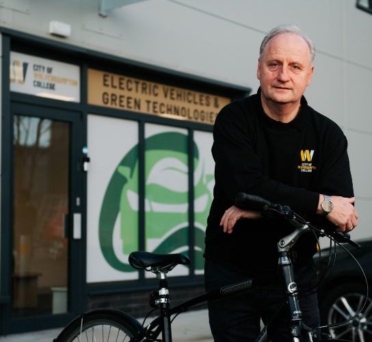 Tutor Paul Mangan wearing a black college sweatshirt, pictured with his bike outside the college's Electric Vehicle training centre