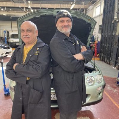 Pete (left) and Kieron Takyar, both wearing blue overalls, in the automotive workshop at the Paget Road campus