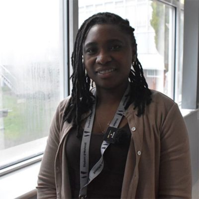 Tapiwa Hakutangwi, wearing a black shirt and brown jacket standing in front of a window