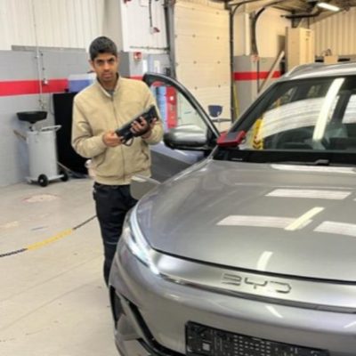 Student Reaz Kausmally wearing a cream jumper standing next to a sliver car