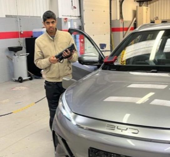 Student Reaz Kausmally wearing a cream jumper standing next to a sliver car